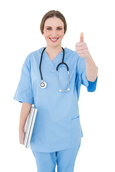 Young female doctor holding a white notebook and putting thumbs up — Stock fotografie