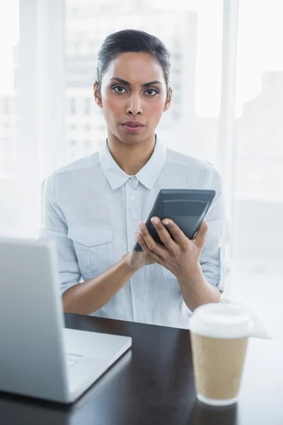 Stern young businesswoman holding a calculator sitting at her de — Stock Photo, Image