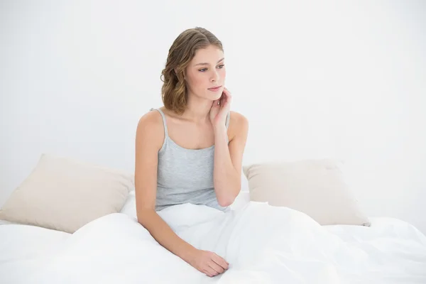 Thoughtful slender woman sitting under the cover on her bed — Stock Photo, Image