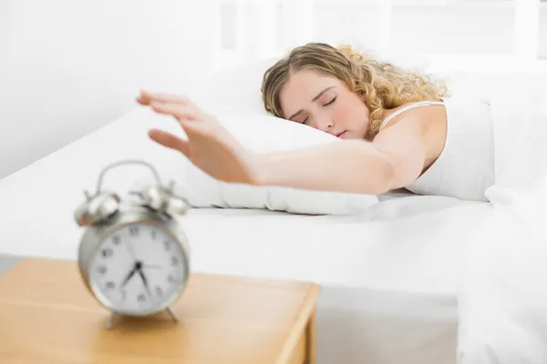 Pretty upset blonde lying in bed reaching for alarm clock — Stock Photo, Image