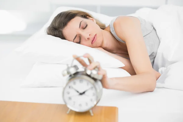 Lovely woman turning off the alarm clock with eyes closed — Stock Photo, Image