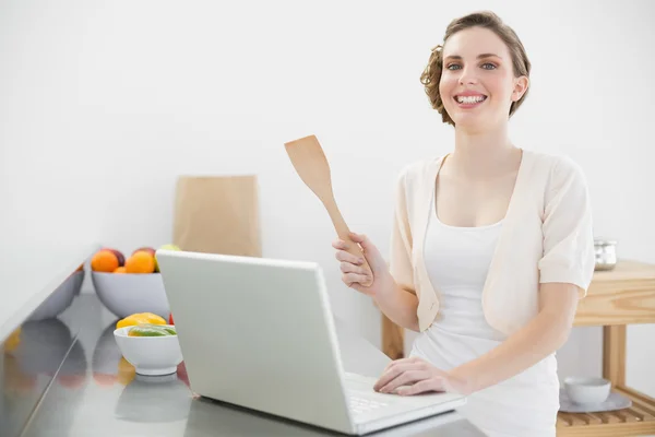 Mulher alegre usando seu caderno de pé na cozinha — Fotografia de Stock