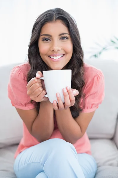 Glad söt brunett sitter på soffan håller mugg — Stockfoto