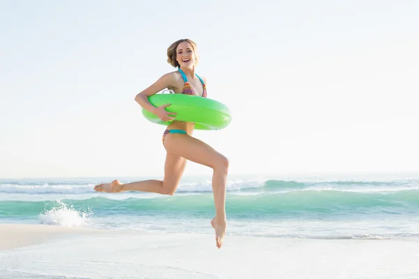 Preciosa mujer joven sosteniendo un anillo de goma mientras salta a la playa — Foto de Stock