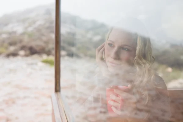 Mujer pensativa con taza de café mirando a través de la ventana — Foto de Stock