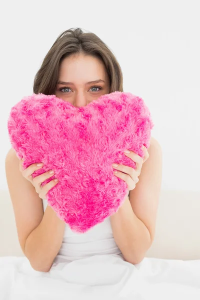 Woman holding heart shaped pillow in bed — Stock Photo, Image