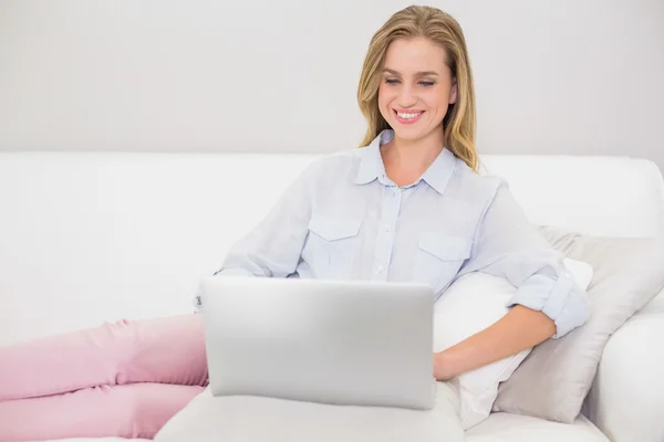 Счастливая блондинка расслабляется на диване с помощью ноутбука — стоковое фото