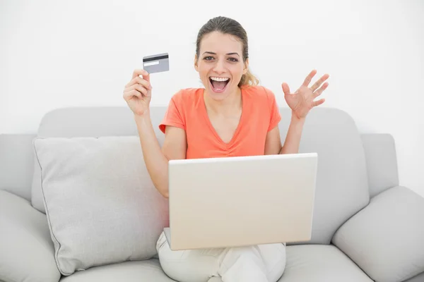 Mulher casual feliz mostrando seu cartão de crédito usando seu caderno — Fotografia de Stock