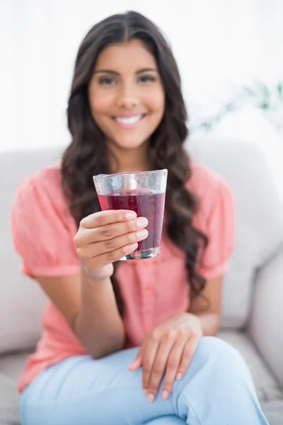 Uśmiechający się ładny brunetka siedzi na kanapie, trzymając szklankę soku — Zdjęcie stockowe