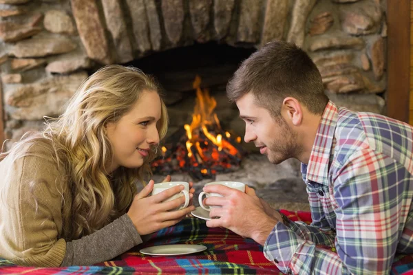 Pareja con tazas de té frente a la chimenea encendida — Foto de Stock