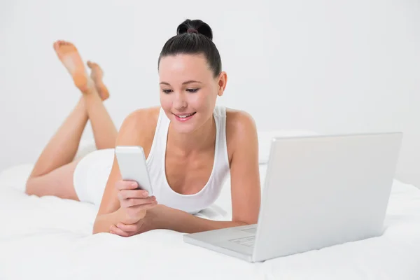 Smiling casual woman using cellphone in bed — Stock Photo, Image