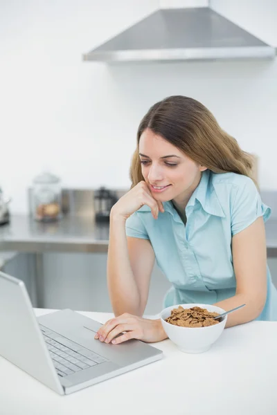 Zufriedene junge Frau, die mit ihrem Laptop in der Küche steht — Stockfoto