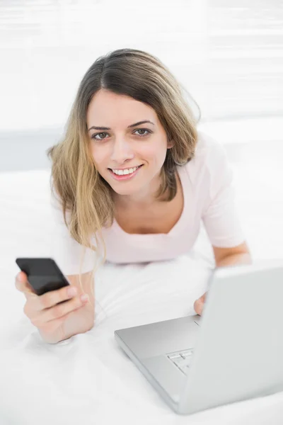 Linda mujer sonriente sosteniendo su teléfono inteligente mirando a la cámara —  Fotos de Stock
