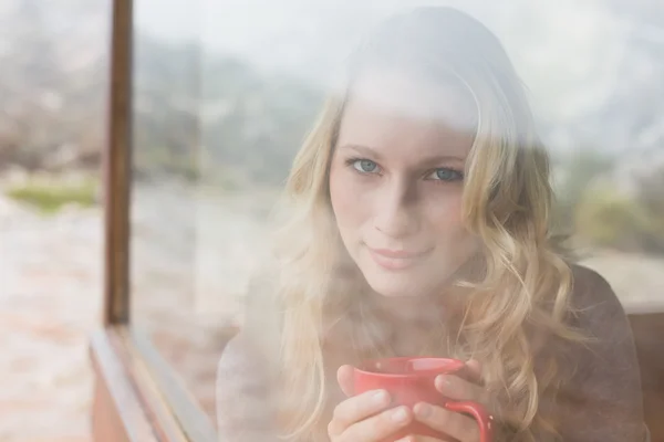 Innehåll kvinna med kaffekopp tittar genom fönstret — Stockfoto