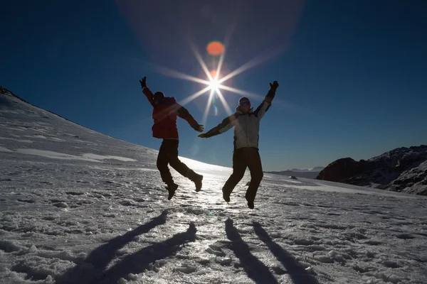 Silhouette couple jumping on snow against sun and blue sky — Stock Photo, Image