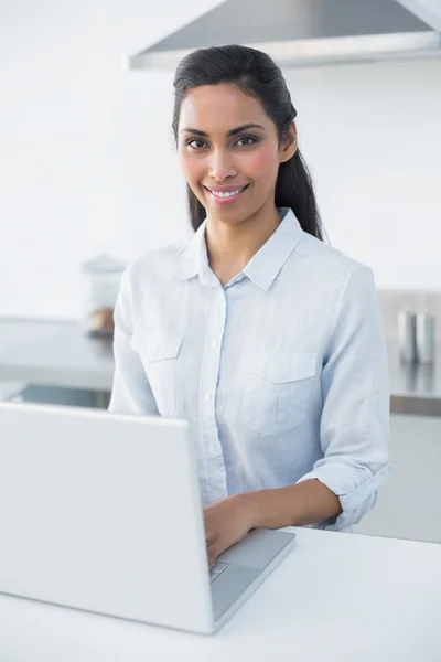 Mujer sonriente contenta escribiendo en su portátil sonriendo a la cámara —  Fotos de Stock