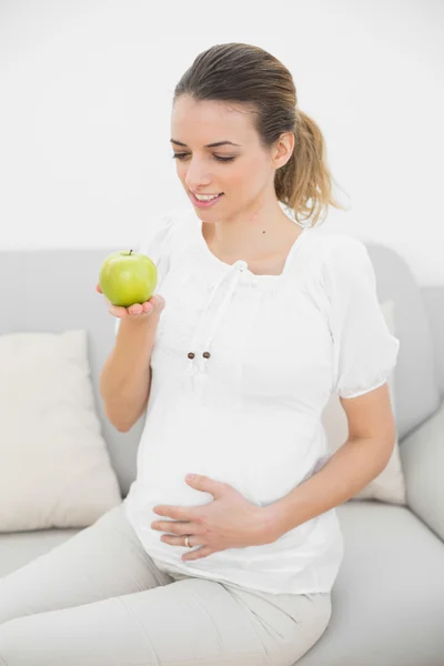 Smiling pregnant woman looking at green apple — Stock Photo, Image