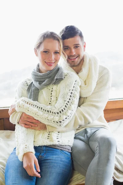 Couple in winter clothing sitting against window — Stock Photo, Image