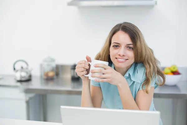 Mujer sonriente alegre sosteniendo una taza posando en su cocina —  Fotos de Stock