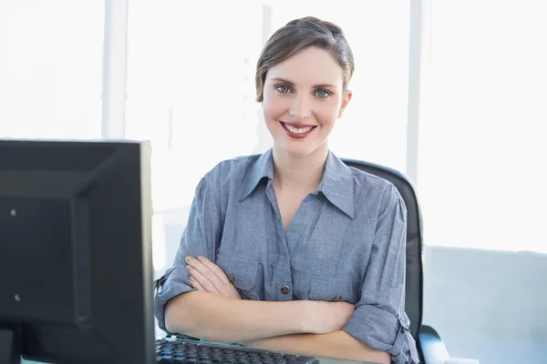 Nette junge Geschäftsfrau sitzt mit verschränkten Armen an ihrem Schreibtisch — Stockfoto