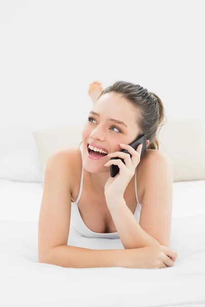 Glada casual kvinna med mobiltelefon i sängen — Stockfoto