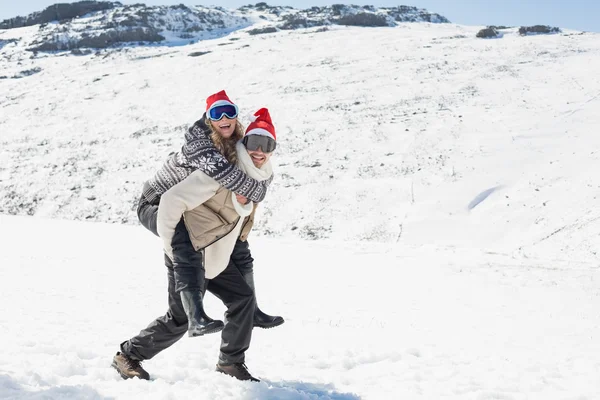 Lunghezza completa di un uomo a cavalluccio donna allegra sulla neve — Foto Stock