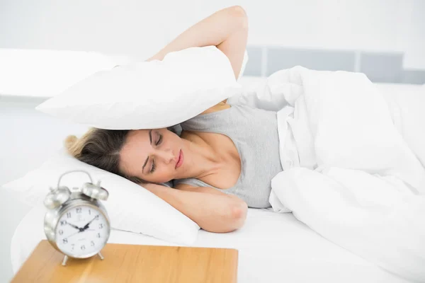 Cute tired woman covering her ears with pillows — Stock Photo, Image