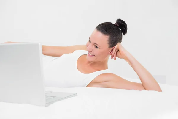 Casual smiling woman looking at laptop in bed — Stock Photo, Image