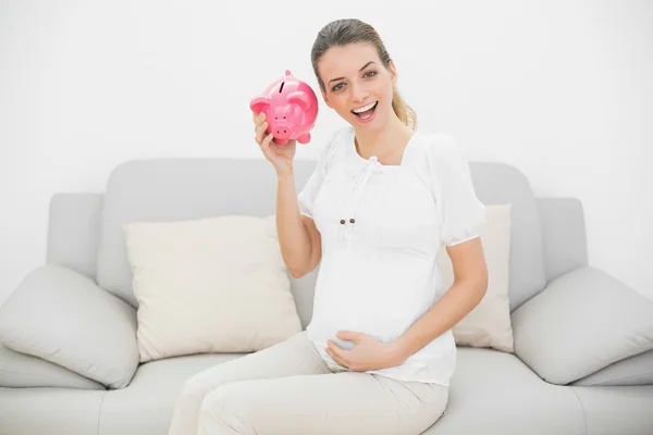 Mulher grávida feliz sacudindo um banco piggy rosa — Fotografia de Stock