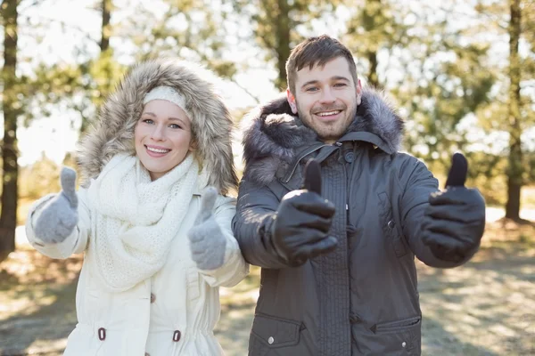 Couple in jackets gesturing thumbs up in the woods — Stock Photo, Image