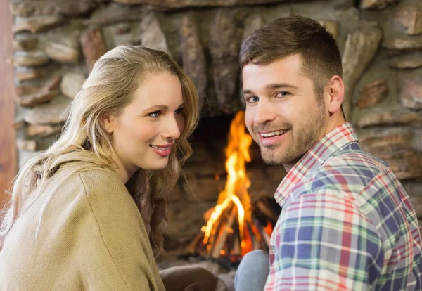 Smiling young couple in front of lit fireplace — Stock Photo, Image