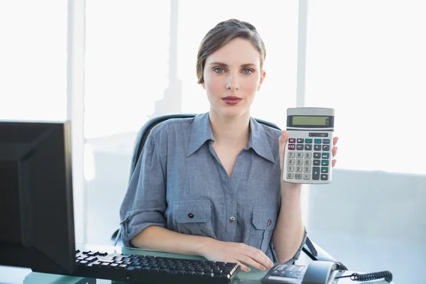 Спокойная деловая женщина показывает калькулятор сидя за столом — стоковое фото