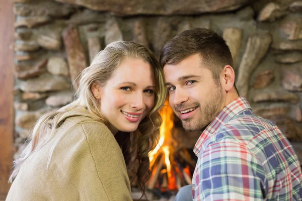 Smiling young couple in front of lit fireplace — Stock Photo, Image