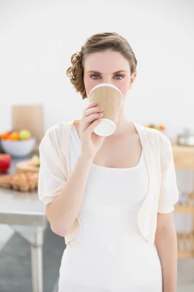 Cute woman standing in kitchen drinking of disposable cup — Stock Photo, Image