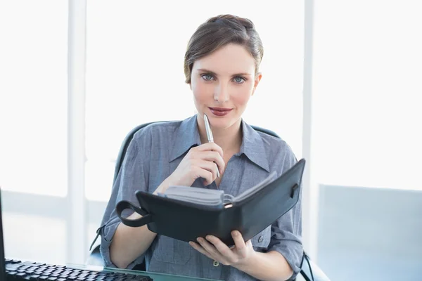 Amable joven mujer de negocios sosteniendo su diario sentado en su escritorio —  Fotos de Stock