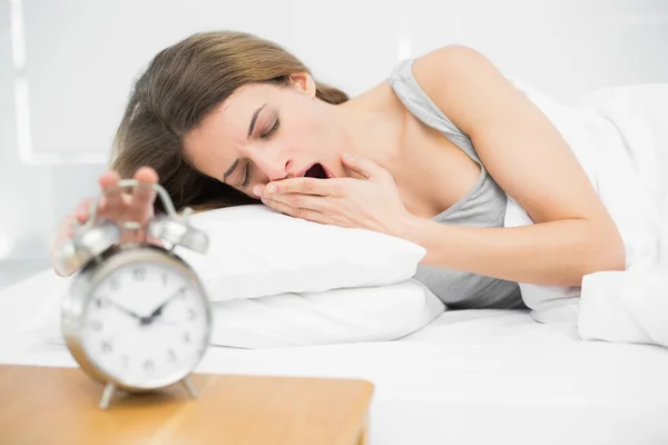 Mujer morena cansada apagando el despertador mientras bosteza —  Fotos de Stock