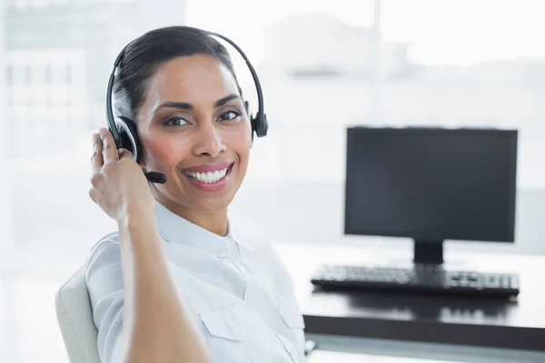 Sorrindo agente feminina vestindo um fone de ouvido sentado em um escritório brilhante — Fotografia de Stock