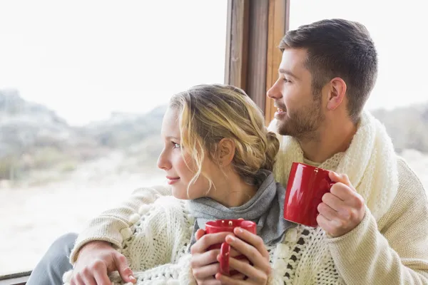 Пара в зимовому одязі з чашками, які виглядають через вікно — стокове фото