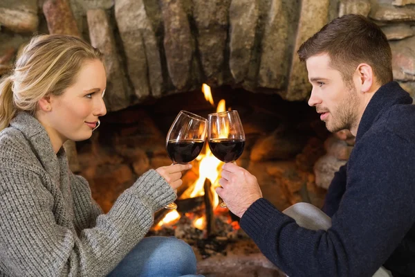 Couple toasting wineglasses in front of lit fireplace — Stock Photo, Image