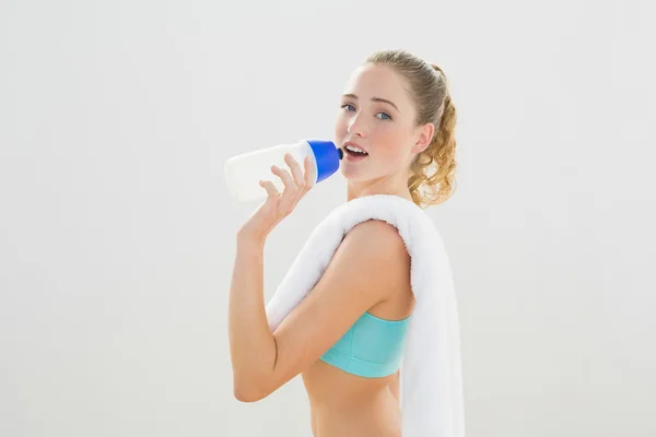 Happy slim blonde standing and drinking from sports bottle — Stock Photo, Image