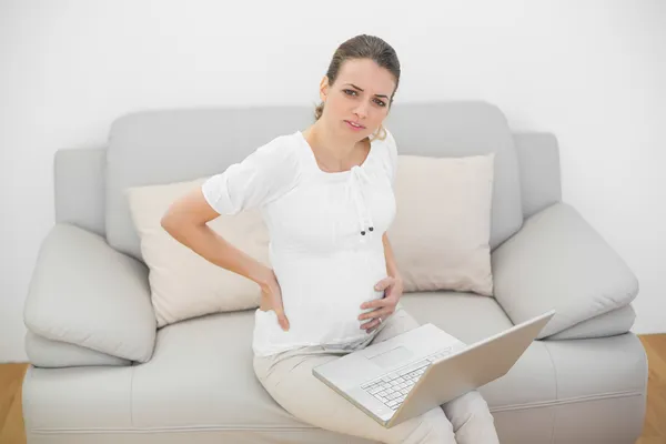 Sufrimiento mujer embarazada tocando su espalda lesionada mirando a la cámara —  Fotos de Stock