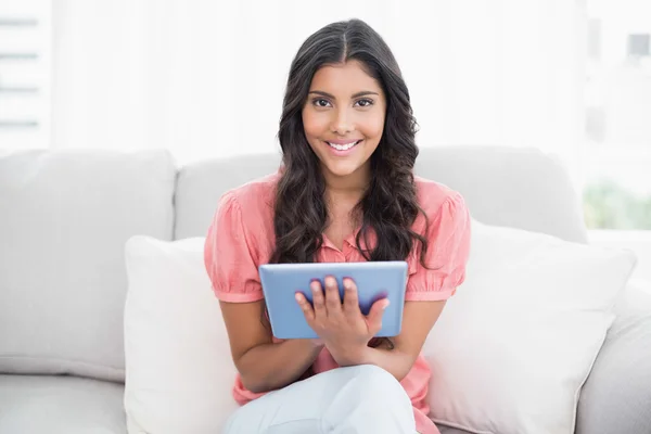 Happy cute brunette sitting on couch using tablet — Stock Photo, Image