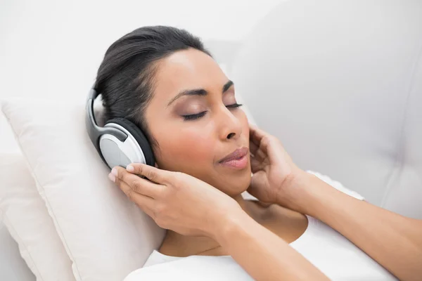 Наслаждаюсь естественной женщиной, слушающей музыку, лежащую на диване — стоковое фото