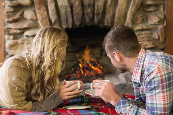 Pareja relajada con tazas de té mirando a la chimenea encendida — Foto de Stock