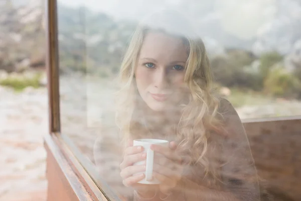 Content woman with coffee cup looking through window — Stock Photo, Image