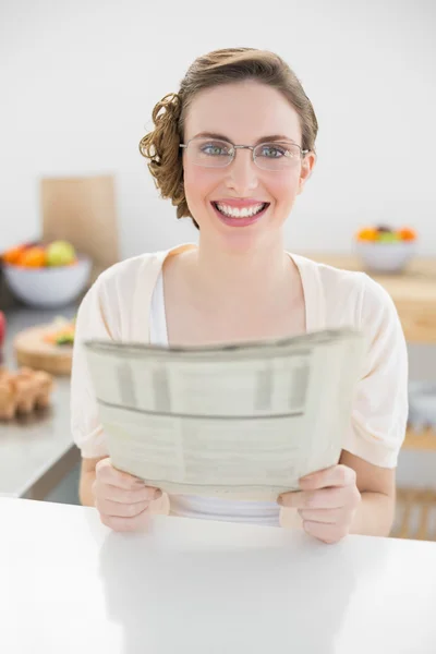 Linda mujer sosteniendo periódico sentado en su cocina — Foto de Stock