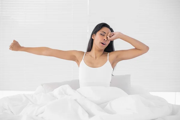 Lovely tired woman stretching out while sitting on her bed — Stock Photo, Image