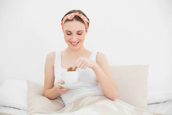 Lächelnde Frau, die einen Keks in ihren Kaffee taucht — Stockfoto