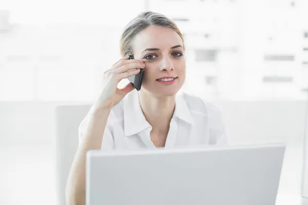 Mujer de negocios suavemente sonriente sentada en su escritorio mientras llama — Foto de Stock