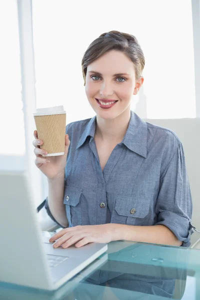 Содержательная деловая женщина показывает одноразовую чашку сидя за своим столом — стоковое фото